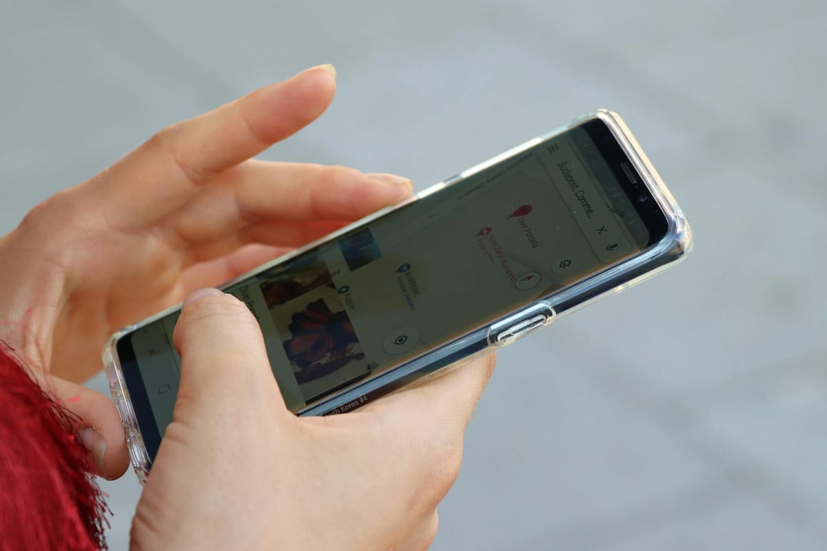 mains tenant un smartphone affichant Google Maps avec marqueurs rouges de commerces locaux lors d'une recherche en extérieur